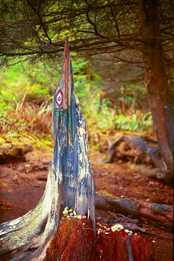 Tree trunk painted in the native style on the beach front with small colored stone gifts of respect.